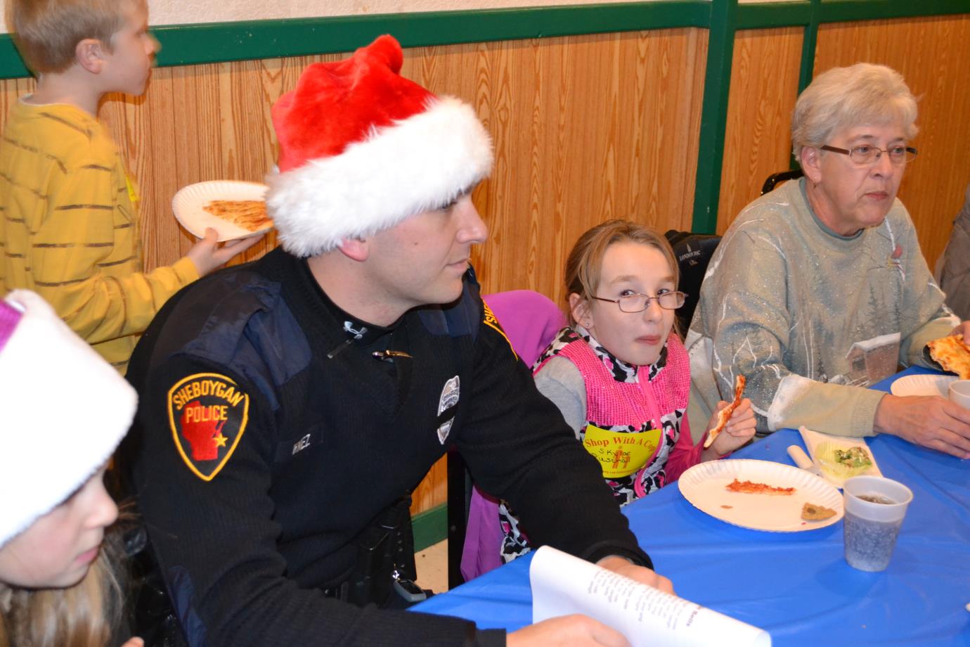 Officer wearing Santa hat while girl nearby laughs